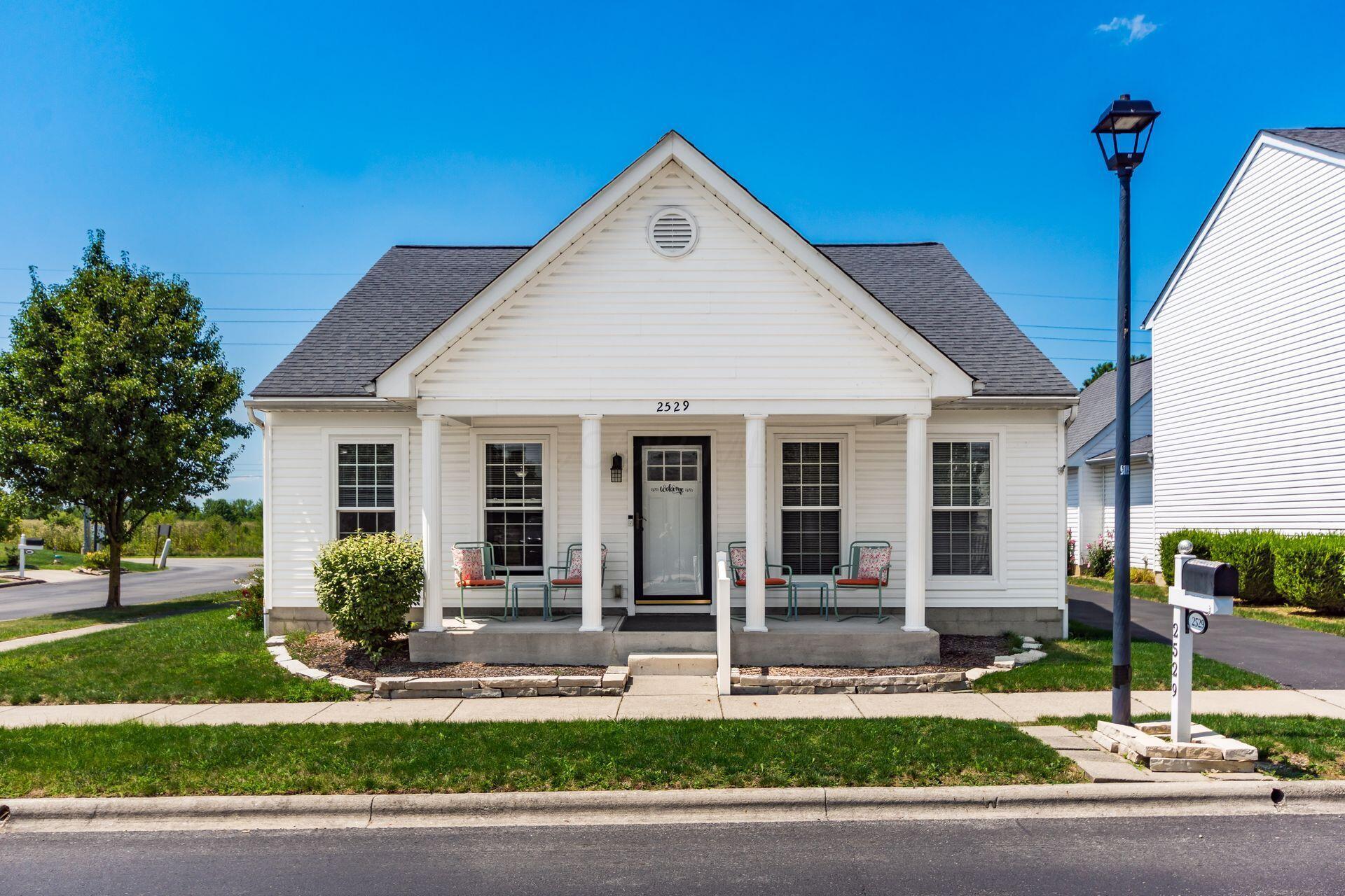 White cottage-style single family home at 2529 Delowe Street in Grove City, Ohio, with a covered front porch, columns and porch chairs