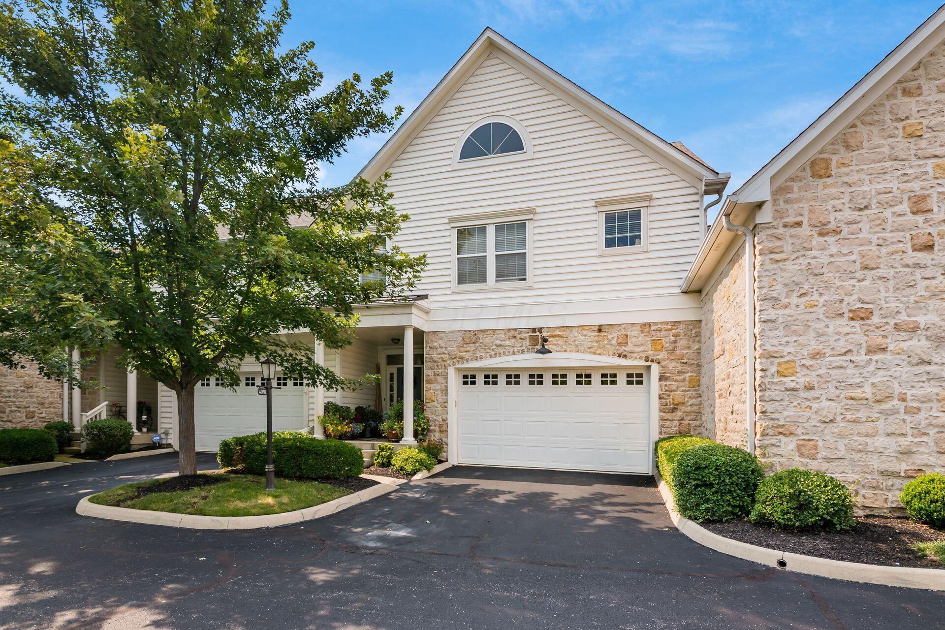 Cream-sided Dublin townhome with a stone-faced garage wing, arched attic window, columned porch and a shade tree over the driveway