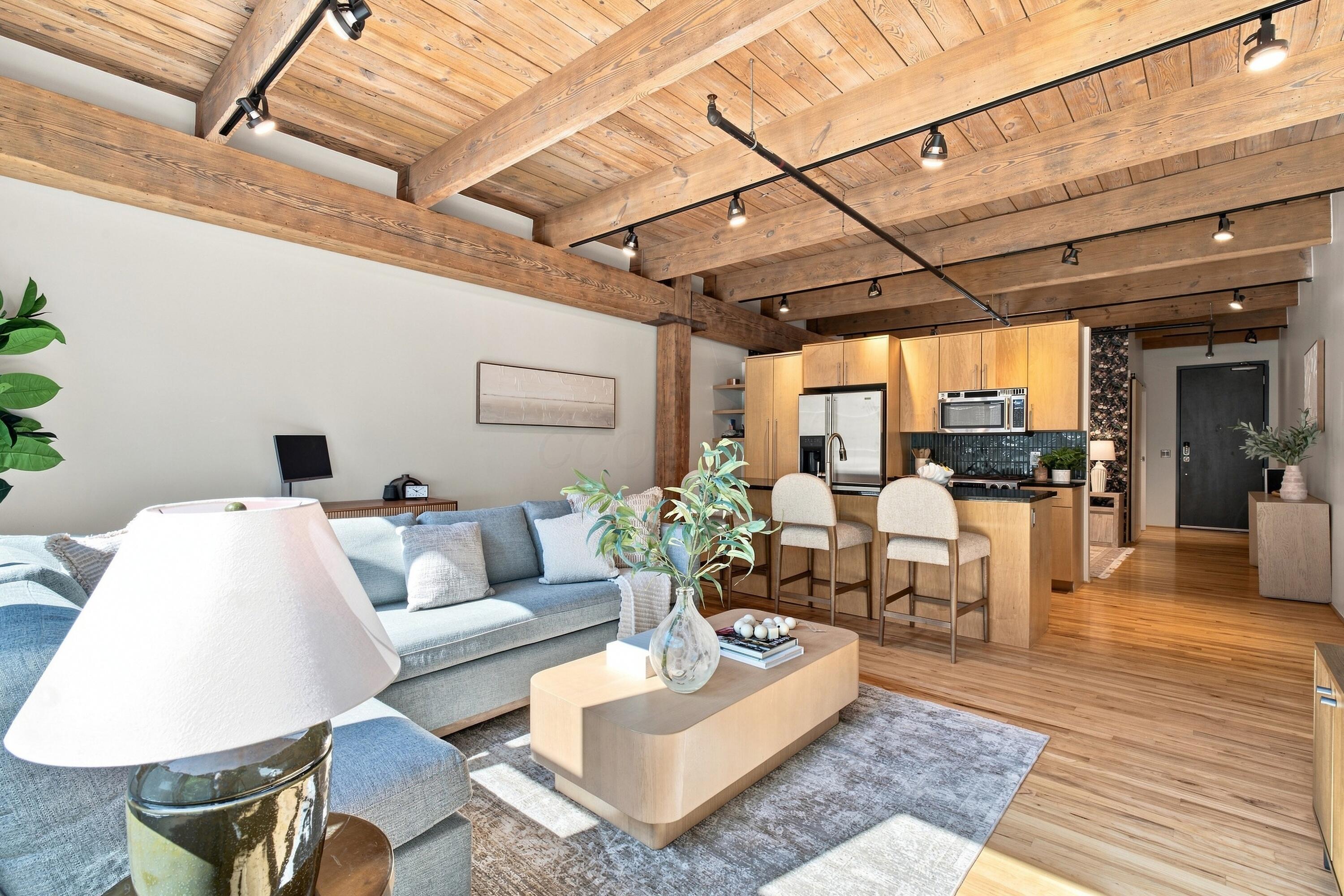 Open-plan loft living room with exposed timber beams, track lighting, hardwood floors and a kitchen island