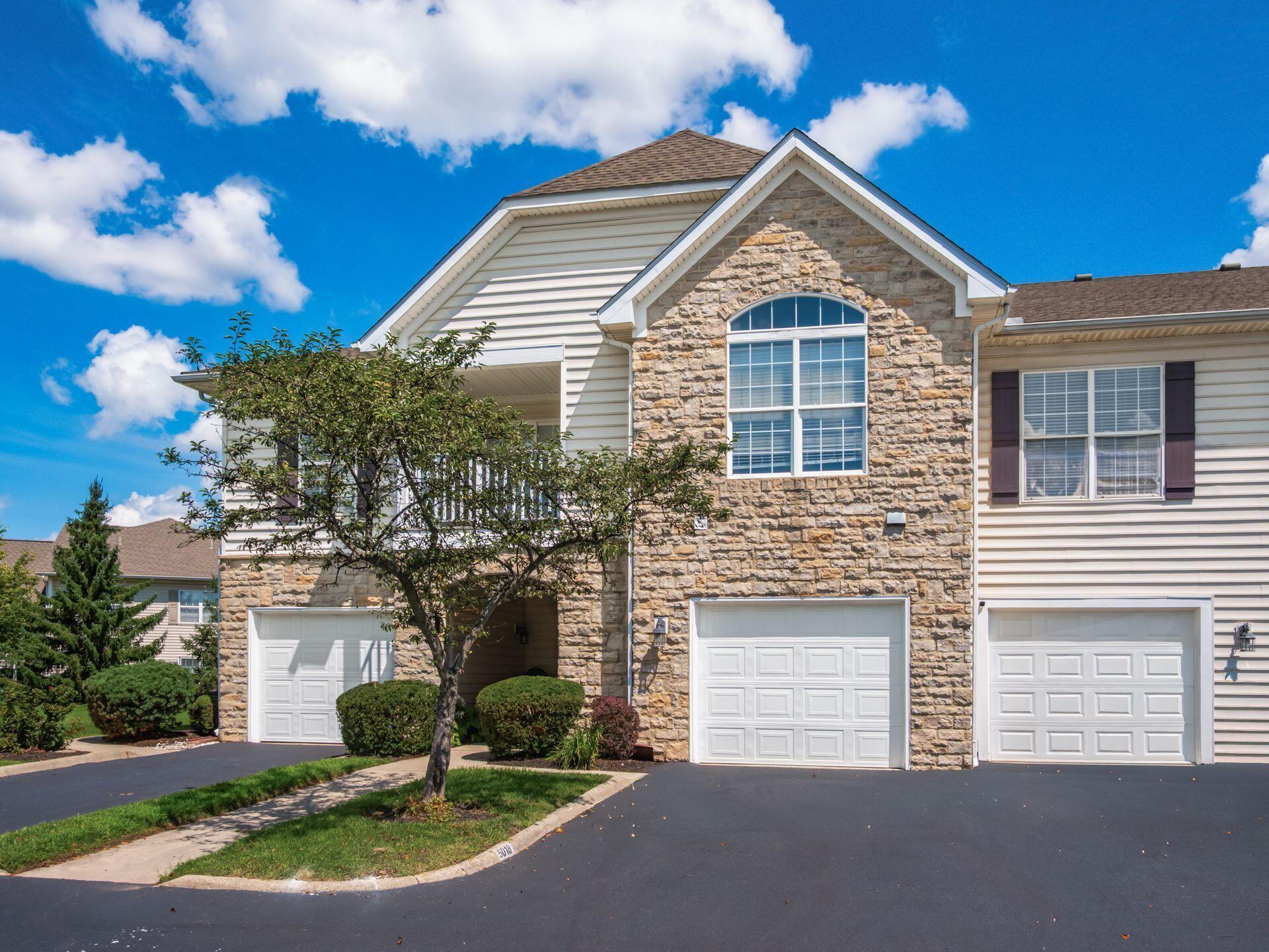 Two-story Dublin condominium at 5018 Ivyvine Boulevard with cream siding, a stone-clad gable, arched window and attached garage