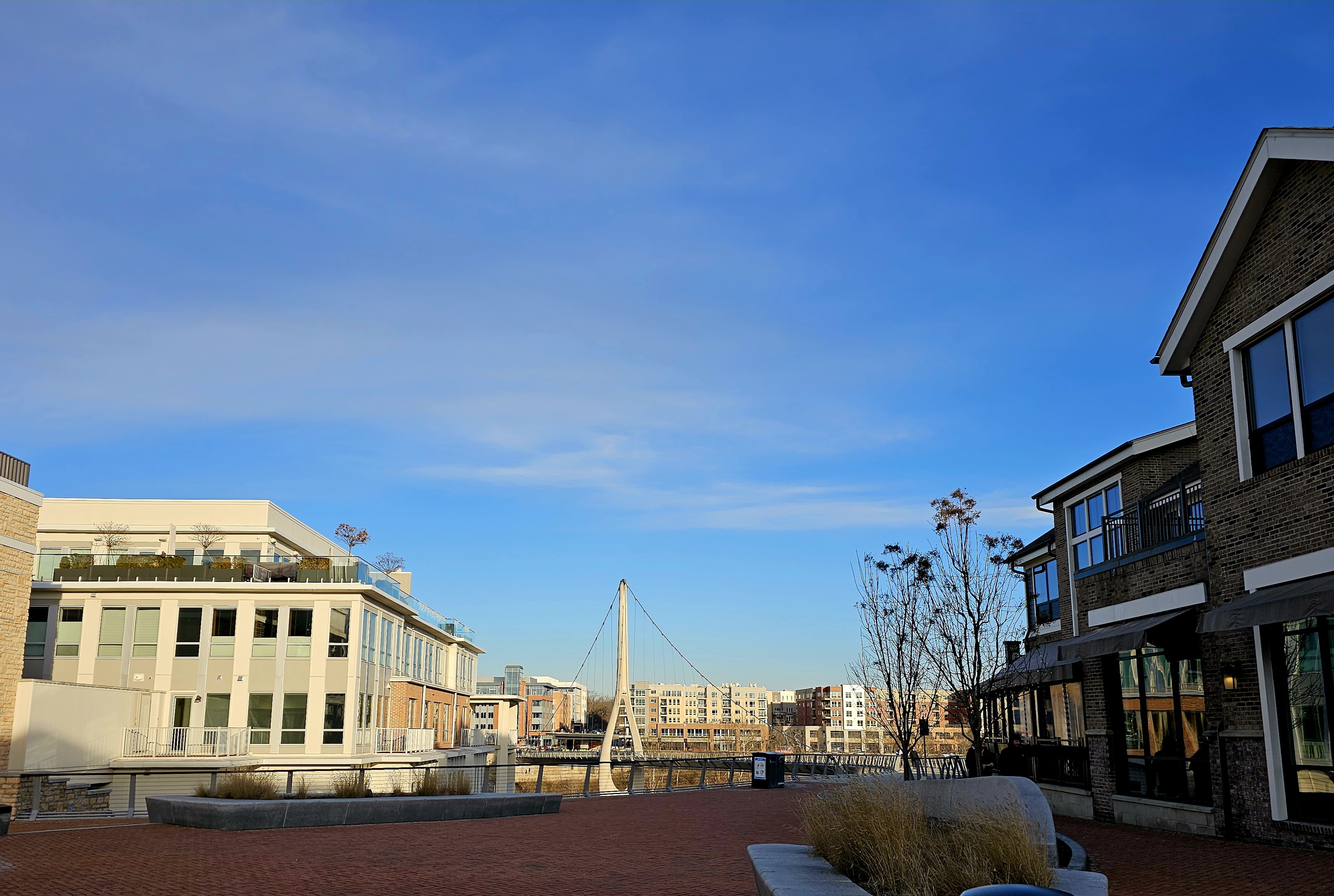 A brick plaza in Bridge Park, Dublin, framed by condominium buildings and restaurant patios, with the tower of the Dublin Link bridge visible at the end of the street