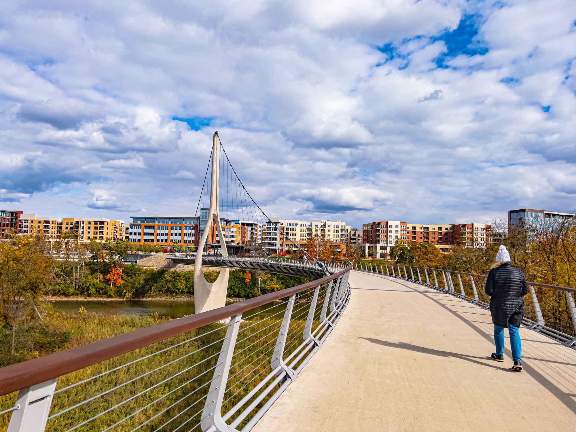 A walker crosses the Dublin Link pedestrian bridge toward Bridge Park in Dublin, Ohio, on an autumn afternoon.
